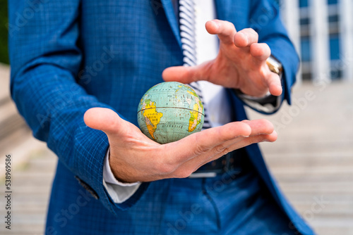 Crop of hands of elegantly dressed executive man holding a globe of the world with one hand and trying to imprison it with the other hand