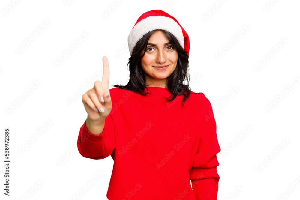 Young Indian woman celebrating Christmas wearing a santa hat isolated showing number one with finger. Young Indian woman celebrating Christmas wearing a santa hat isolated showing number one with finger.