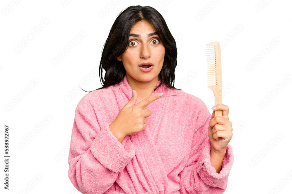 Young woman in a bathrobe holding an hair comb isolated pointing to the side Young woman in a bathrobe holding an hair comb isolated pointing to the side