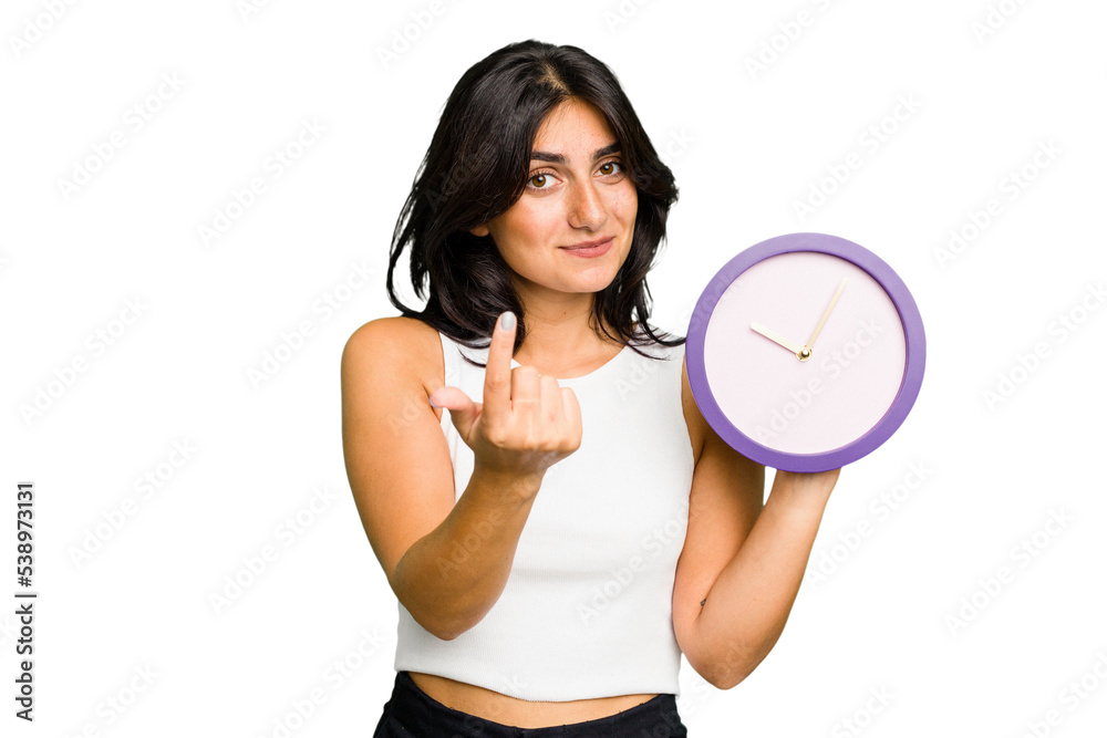 Young Indian woman holding a clock isolated pointing with finger at you as if inviting come closer. Young Indian woman holding a clock isolated pointing with finger at you as if inviting come closer.