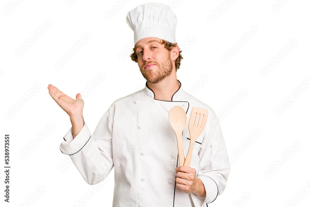 Young cook man isolated on white background showing a copy space on a palm and holding another hand on waist. Young cook man isolated on white background showing a copy space on a palm and holding another hand on waist.