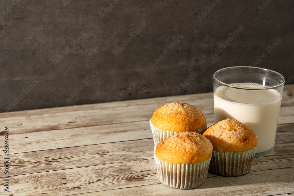 Glass of milk with three freshly baked muffins in the foreground - breakfast, snack, pastries concept Glass of milk with three freshly baked muffins in the foreground - breakfast, snack, pastries concept