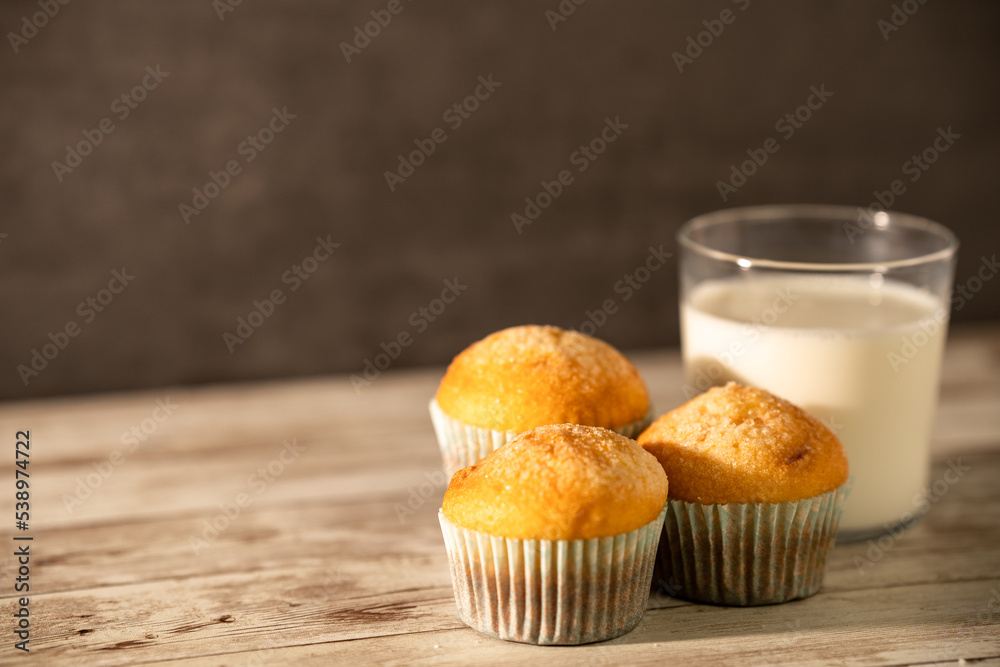 Glass of milk with three freshly baked muffins in the foreground - breakfast, snack, pastries concept Glass of milk with three freshly baked muffins in the foreground - breakfast, snack, pastries concept