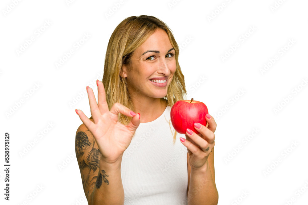 Young caucasian woman holding an apple isolated on green chroma background cheerful and confident showing ok gesture. Young caucasian woman holding an apple isolated on green chroma background cheerful and confident showing ok gesture.