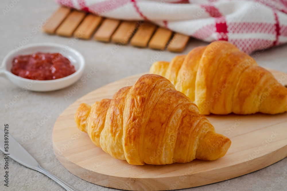 Fresh croissant on wooden board and jam on table