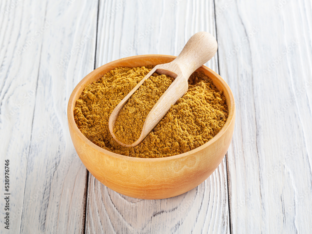 Curry powder in wooden bowl on white wooden background Curry powder in wooden bowl on white wooden background