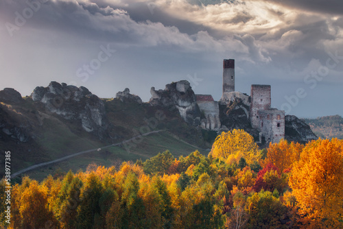 Olsztyn Castle in Autumn with colorful trees in the foreground and cloudy sky.