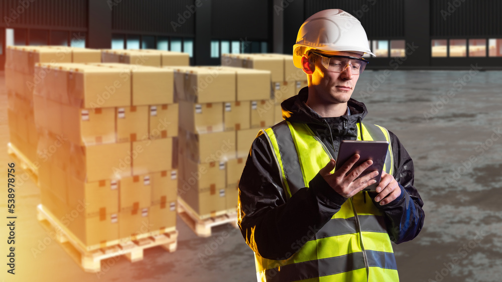 Warehouse worker. Man works in warehouse for delivery service. Delivery boxes behind guy. Man with electronic tablet in hangar. Empty hangar with delivery boxes. Storekeeper Career. Art focus