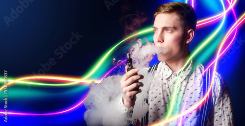 Man smokes vape. Guy with electronic cigarette. Vape cigarette in hands of man. Smoker is holding vape device. Party-goer blows smoke from his mouth. Smoking student with neon stripes