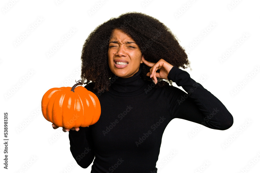 Young African American woman holding a pumpkin for halloween day isolated covering ears with hands. Young African American woman holding a pumpkin for halloween day isolated covering ears with hands.