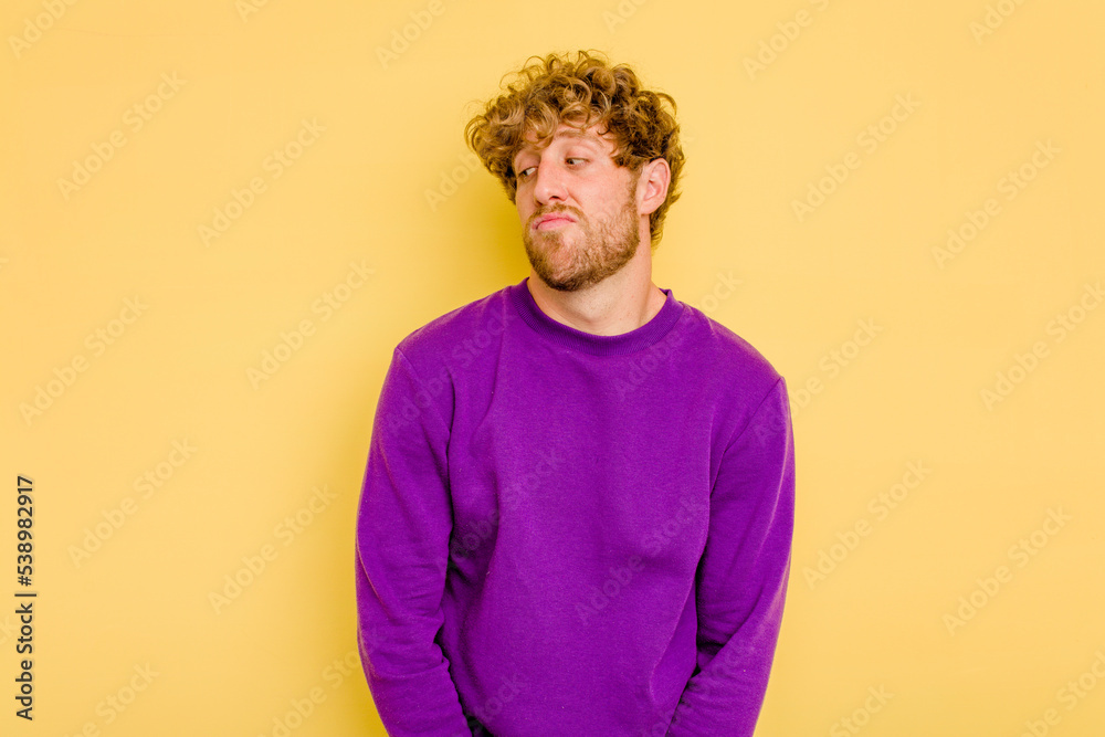 Young caucasian man isolated on yellow background shrugs shoulders and open eyes confused. Young caucasian man isolated on yellow background shrugs shoulders and open eyes confused.