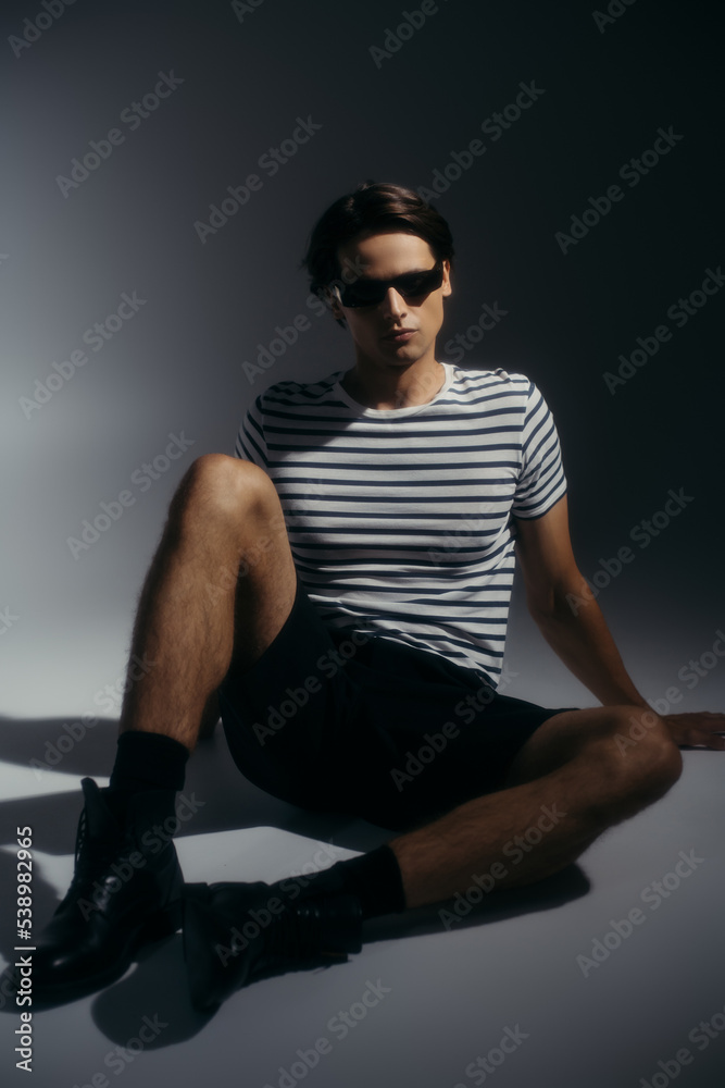 Trendy model in sunglasses and shoes posing on grey background with lighting and shadow