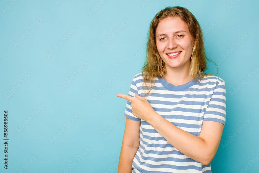 Young caucasian woman isolated on blue background smiling and pointing aside, showing something at blank space. Young caucasian woman isolated on blue background smiling and pointing aside, showing something at blank space.