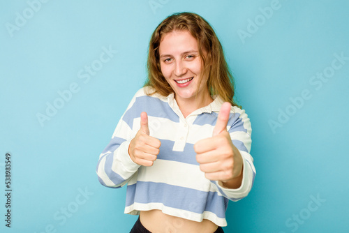 Young caucasian woman isolated on blue background raising both thumbs up, smiling and confident.