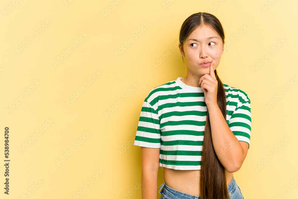 Young Asian woman isolated on yellow background looking sideways with doubtful and skeptical expression. Young Asian woman isolated on yellow background looking sideways with doubtful and skeptical expression.