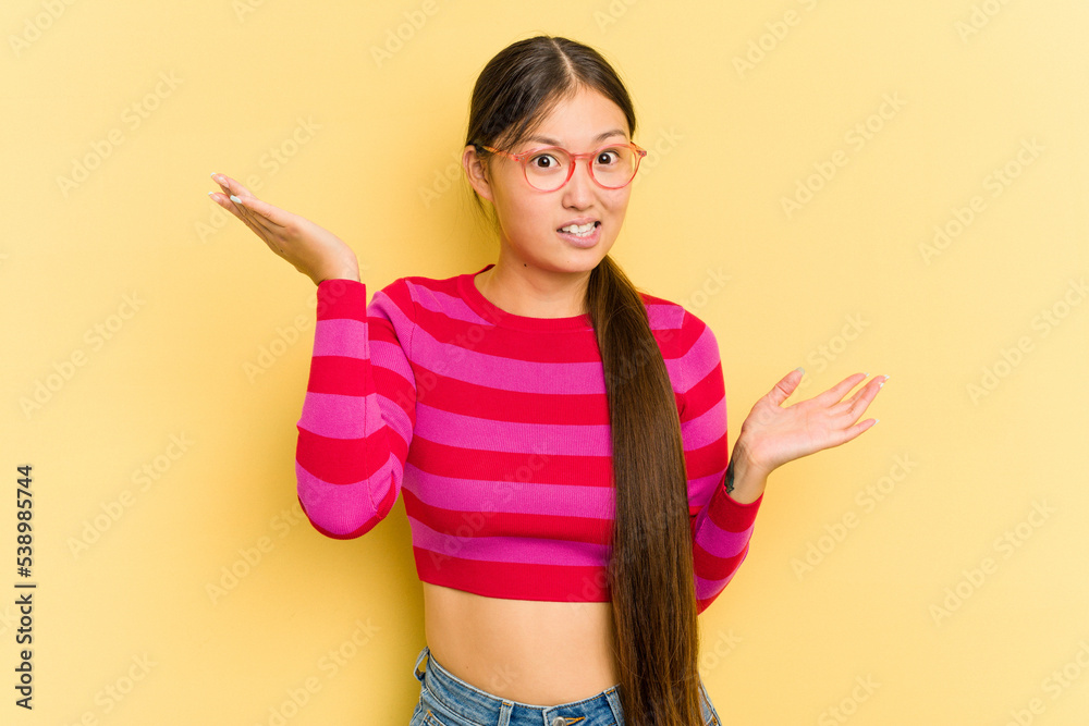Young Asian woman isolated on yellow background confused and doubtful shrugging shoulders to hold a copy space.