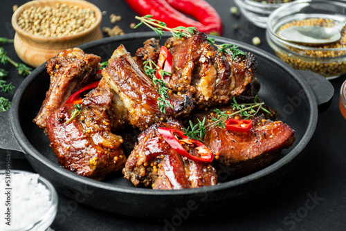 Baked ribs in a pan. Roasted ribs with spices and herbs on a dark background. Food background. Side view. Close-up.