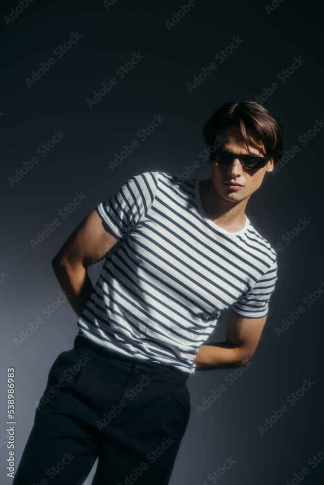 Stylish brunette man in sunglasses posing on grey background