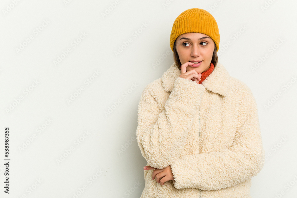 Young Indian woman wearing winter jacket isolated on white background relaxed thinking about something looking at a copy space.