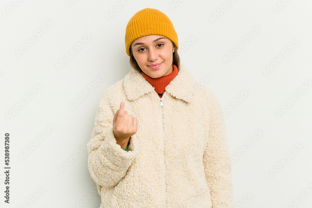 Young Indian woman wearing winter jacket isolated on white background pointing with finger at you as if inviting come closer.