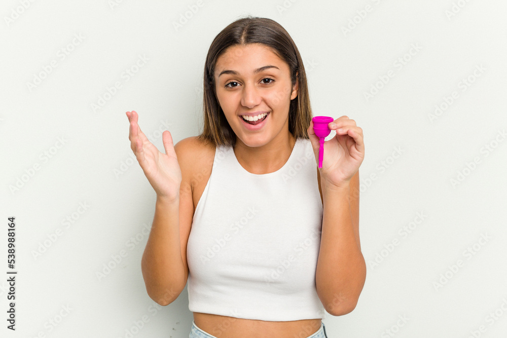 Young woman holding a menstrual cup isolated on white background receiving a pleasant surprise, excited and raising hands. Young woman holding a menstrual cup isolated on white background receiving a pleasant surprise, excited and raising hands.