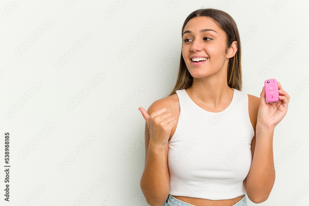 Young indian woman holding an electronic pink car keys points with thumb finger away, laughing and carefree. Young indian woman holding an electronic pink car keys points with thumb finger away, laughing and carefree.