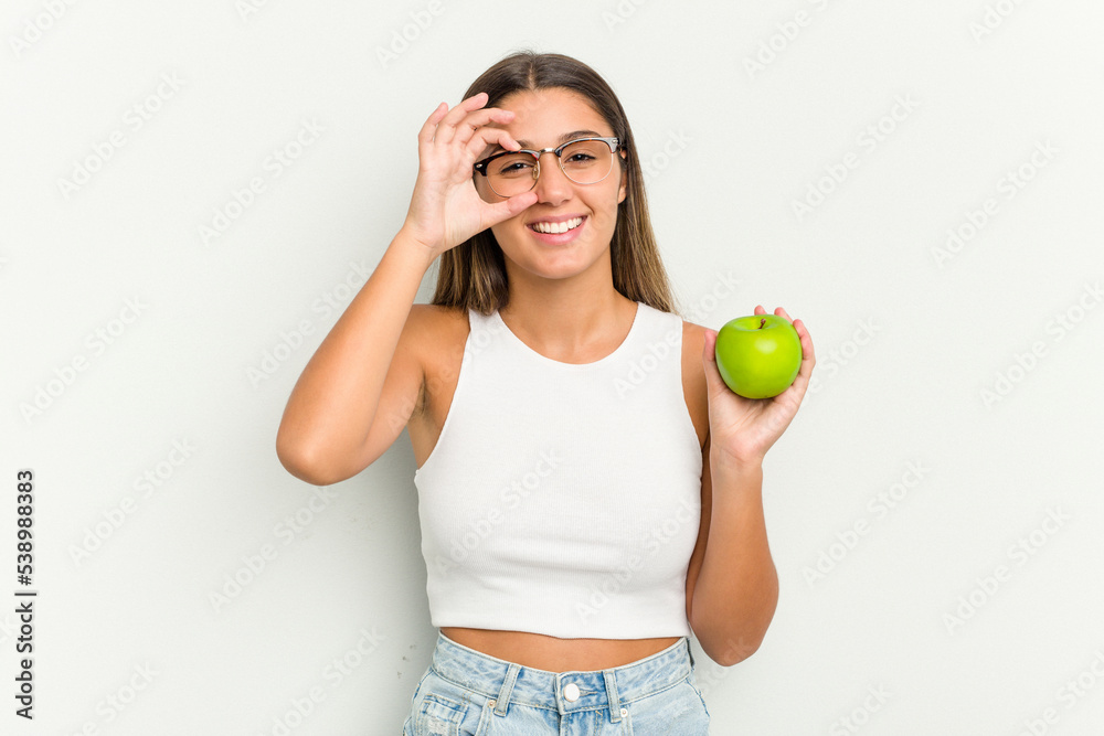 Young Indian woman holding an apple isolated on white background excited keeping ok gesture on eye. Young Indian woman holding an apple isolated on white background excited keeping ok gesture on eye.