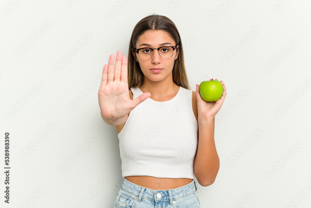 Young Indian woman holding an apple isolated on white background standing with outstretched hand showing stop sign, preventing you. Young Indian woman holding an apple isolated on white background standing with outstretched hand showing stop sign, preventing you.