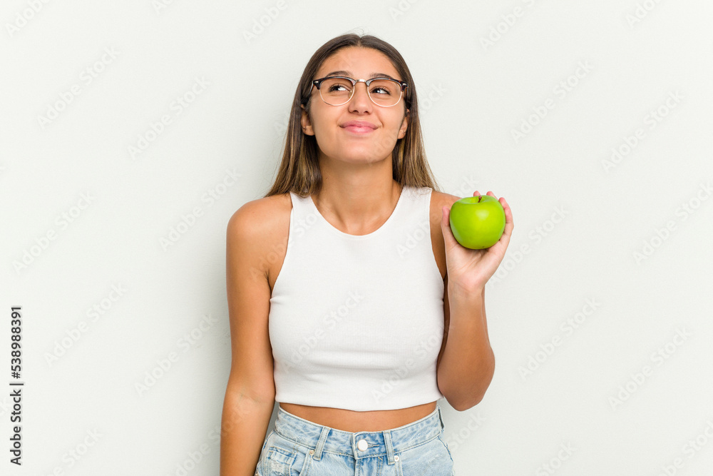 Young Indian woman holding an apple isolated on white background dreaming of achieving goals and purposes