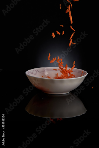 Grated carrots are poured from top to bottom into a white bowl.