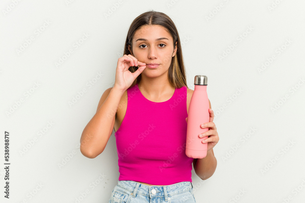 Young indian woman holding a pink thermo isolated on white background with fingers on lips keeping a secret.