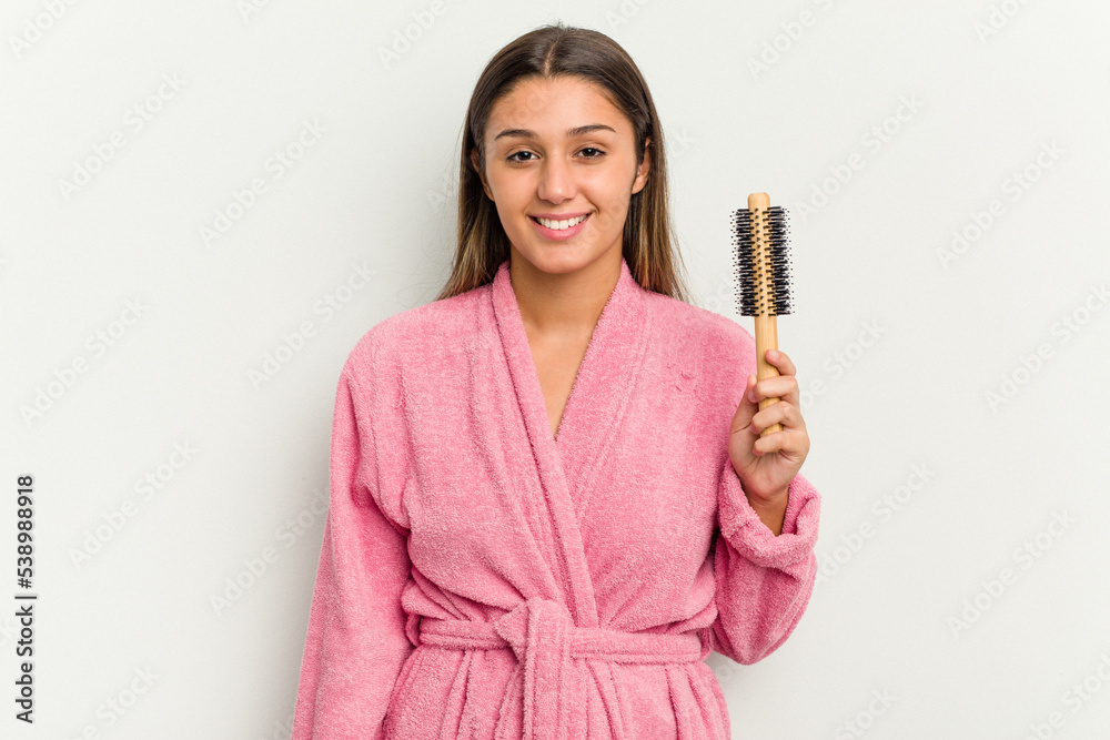 Young Indian woman wearing a bathrobe holding an hairbrush isolated on white background happy, smiling and cheerful. Young Indian woman wearing a bathrobe holding an hairbrush isolated on white background happy, smiling and cheerful.