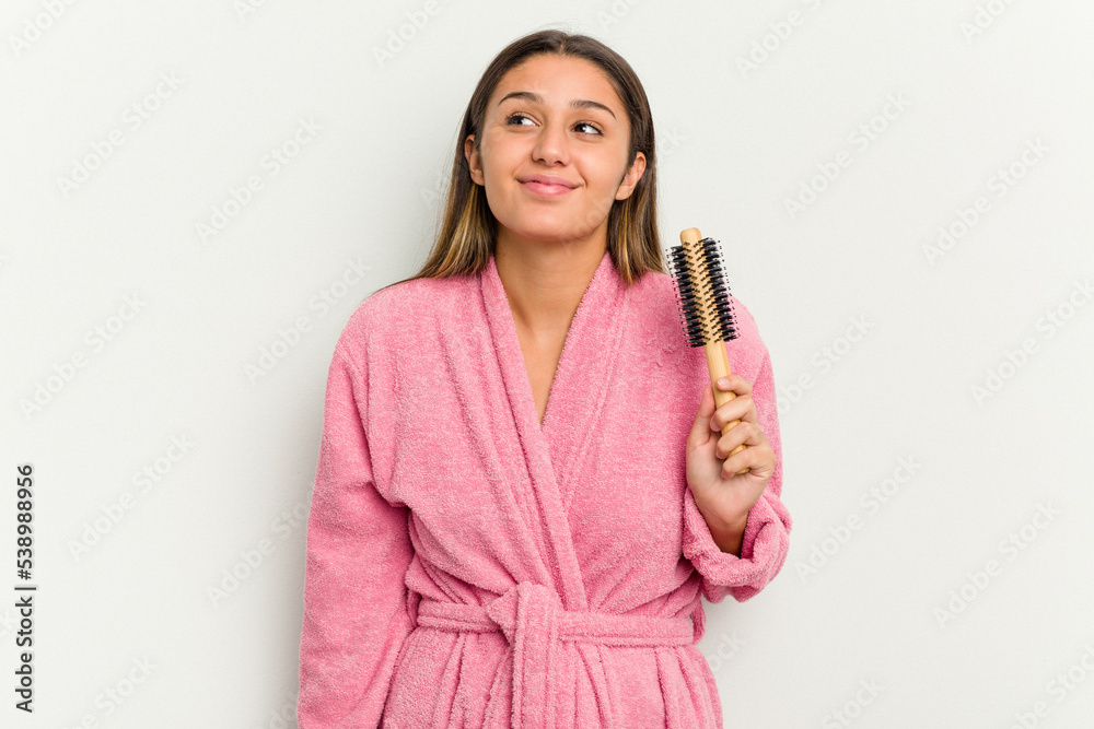 Young Indian woman wearing a bathrobe holding an hairbrush isolated on white background dreaming of achieving goals and purposes Young Indian woman wearing a bathrobe holding an hairbrush isolated on white background dreaming of achieving goals and purposes