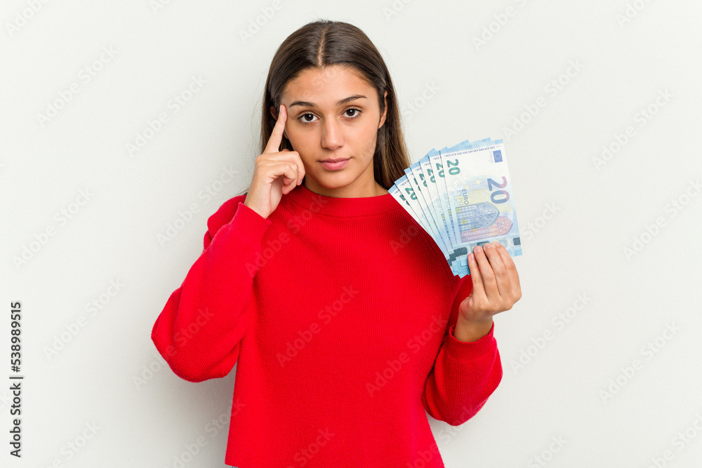 Young Indian woman holding a banknotes isolated on white background pointing temple with finger, thinking, focused on a task. Young Indian woman holding a banknotes isolated on white background pointing temple with finger, thinking, focused on a task.
