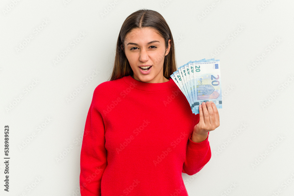 Young Indian woman holding a banknotes isolated on white background screaming very angry and aggressive. Young Indian woman holding a banknotes isolated on white background screaming very angry and aggressive.