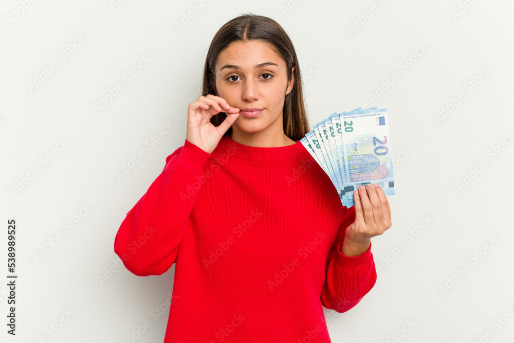 Young Indian woman holding a banknotes isolated on white background with fingers on lips keeping a secret. Young Indian woman holding a banknotes isolated on white background with fingers on lips keeping a secret.