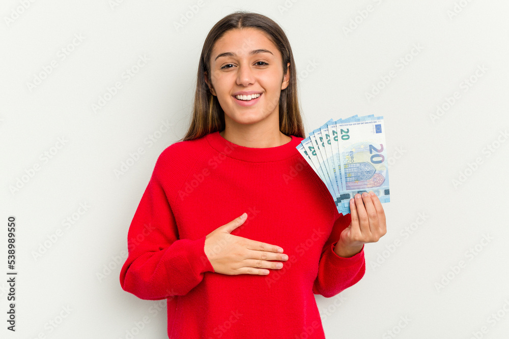 Young Indian woman holding a banknotes isolated on white background laughs out loudly keeping hand on chest. Young Indian woman holding a banknotes isolated on white background laughs out loudly keeping hand on chest.