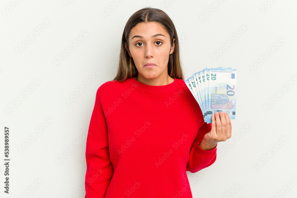 Young Indian woman holding a banknotes isolated on white background shrugs shoulders and open eyes confused. Young Indian woman holding a banknotes isolated on white background shrugs shoulders and open eyes confused.