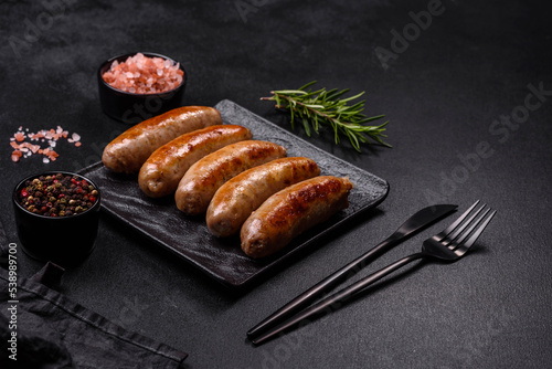 Tasty grilled sausages with spices and herbs on a black slate plate