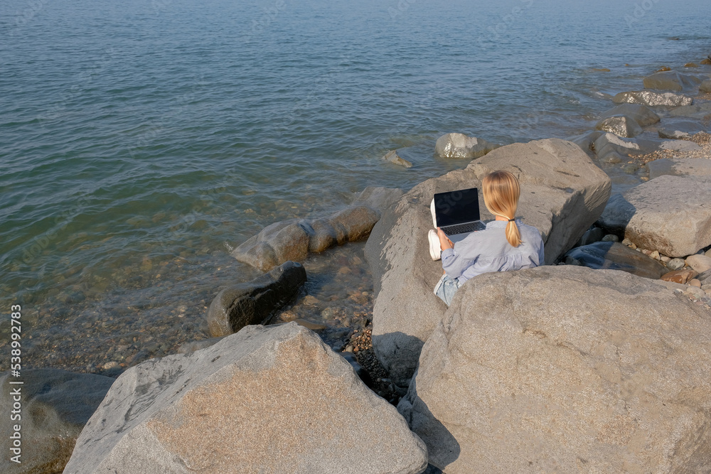 Remote work.Girl freelancer works remotely on the sea shore.workation, remote work,WFVH,Van Life vibes work from vacation home,work travel,remotely work.Travelling.Work from vacation remotely