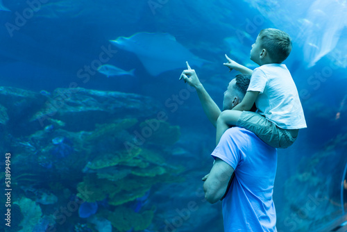 Dad and son spend time together in the Aquarium. Son sits on dad's back and explores the underwater world