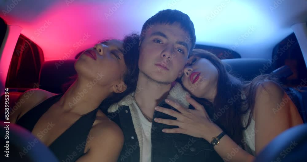 Transportation of passengers in the back seat of a taxi. Polyamorous guy with two girls, focus of attention, open flirting. He will cover his face with his hands - attention fatigue.