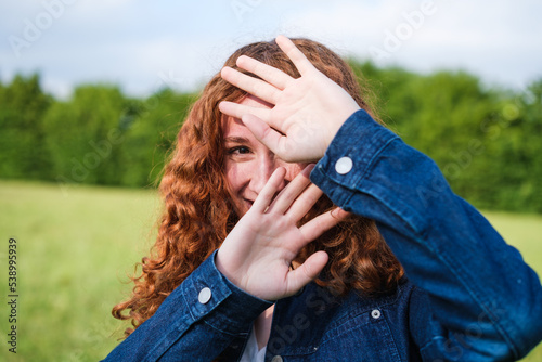 Shy young redhead woman covers her face so as not to appear in the photo outdoors in the park at sunset
