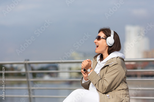 Attractive woman plus size sit on the city embankment and emotionally singing along to music with headphones, selective focus. photo