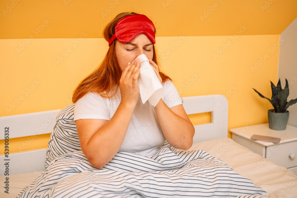 Young depressed or sick with flu pregnant model lying on the bed and blowing her nose into tissue. 