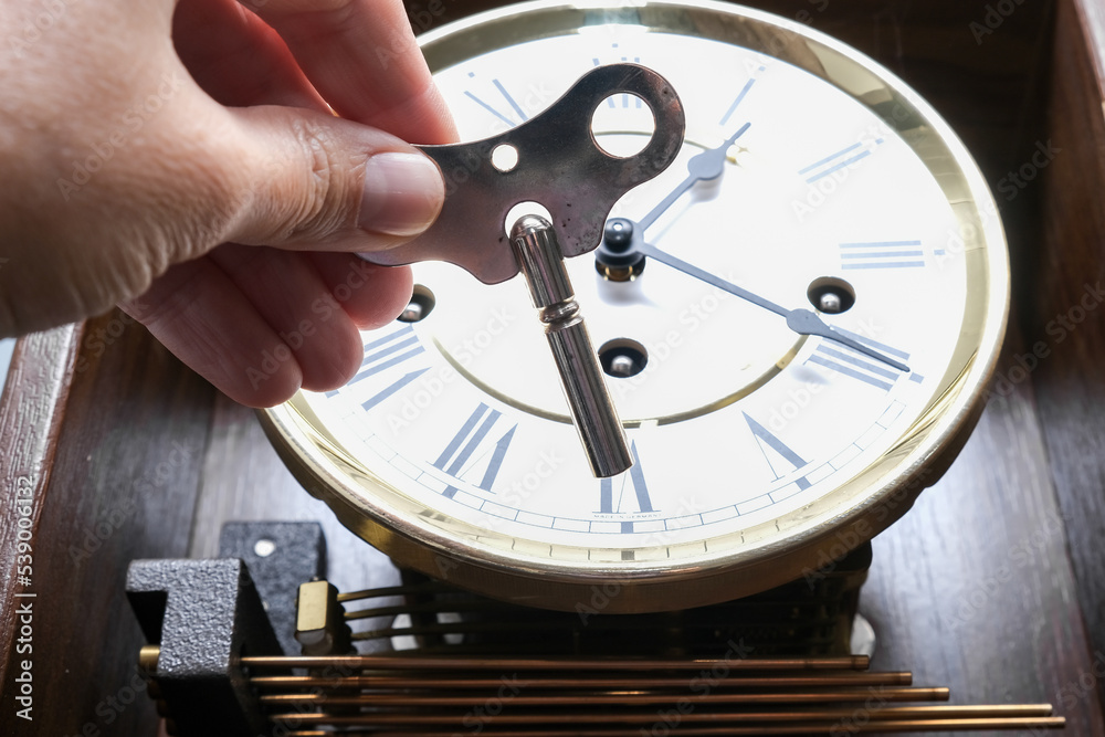 Fototapeta premium A hand holding a key to wind up a clockwork, vintage classic clock mechanism