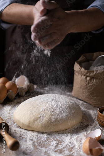 Baker chef man sprinkling flour at dough bread and bakery ingredients for homemade cooking on table