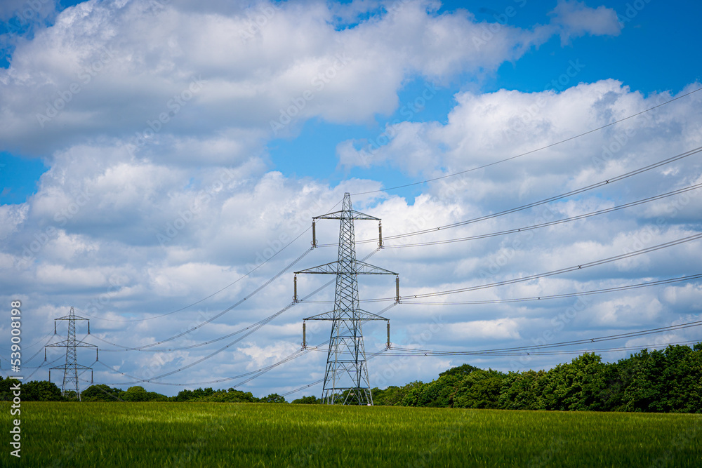 Pylon Power Electricity Electrical Distribution Aerial Cable Running through Countryside Farmer Fields with Blue Sky and White Clouds