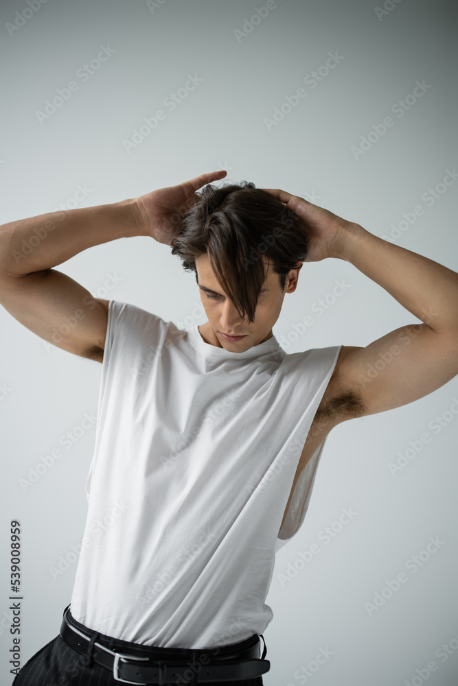 stylish man in white t-shirt adjusting hair while posing on grey stylish man in white t-shirt adjusting hair while posing on grey