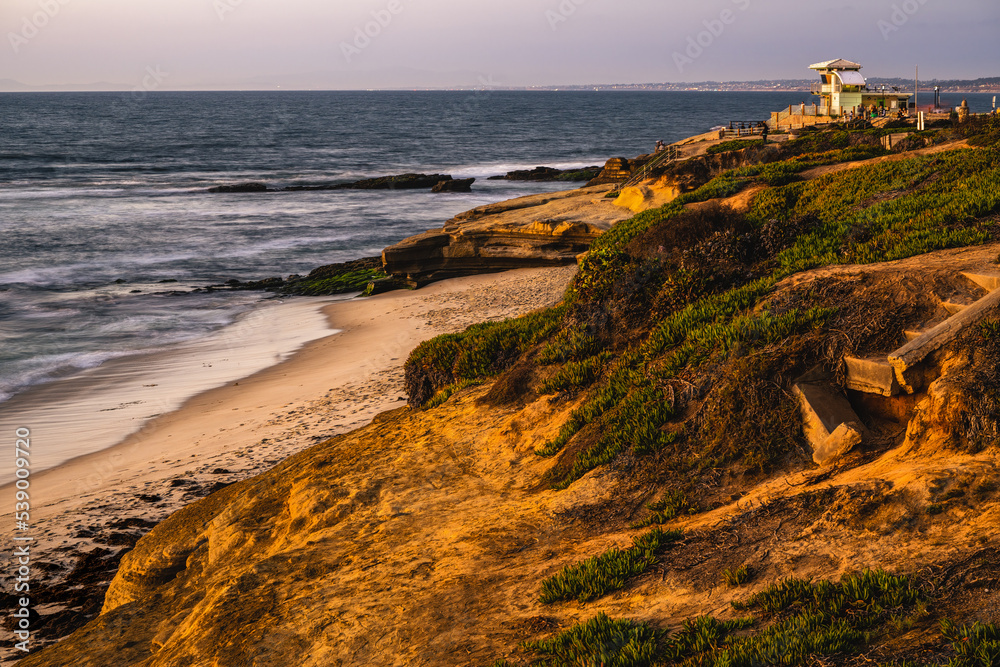 2022-10-17 SHORE LINE IN LA JOLLA WITH ROCKY OUTCROPPING PACIFIC OCEAN WITH BLURRED WAVES AND A LIFE GUARD STATION NEAR SAN DIEGO CALIFORNIA